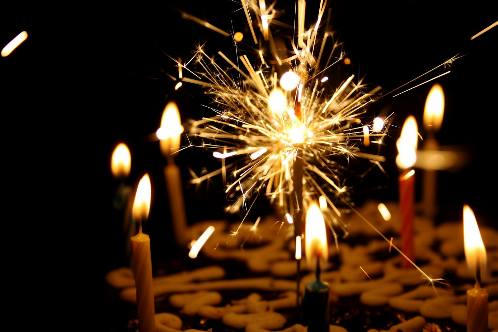 A sparkler burning above a candlelit birthday cake in a darkened room
