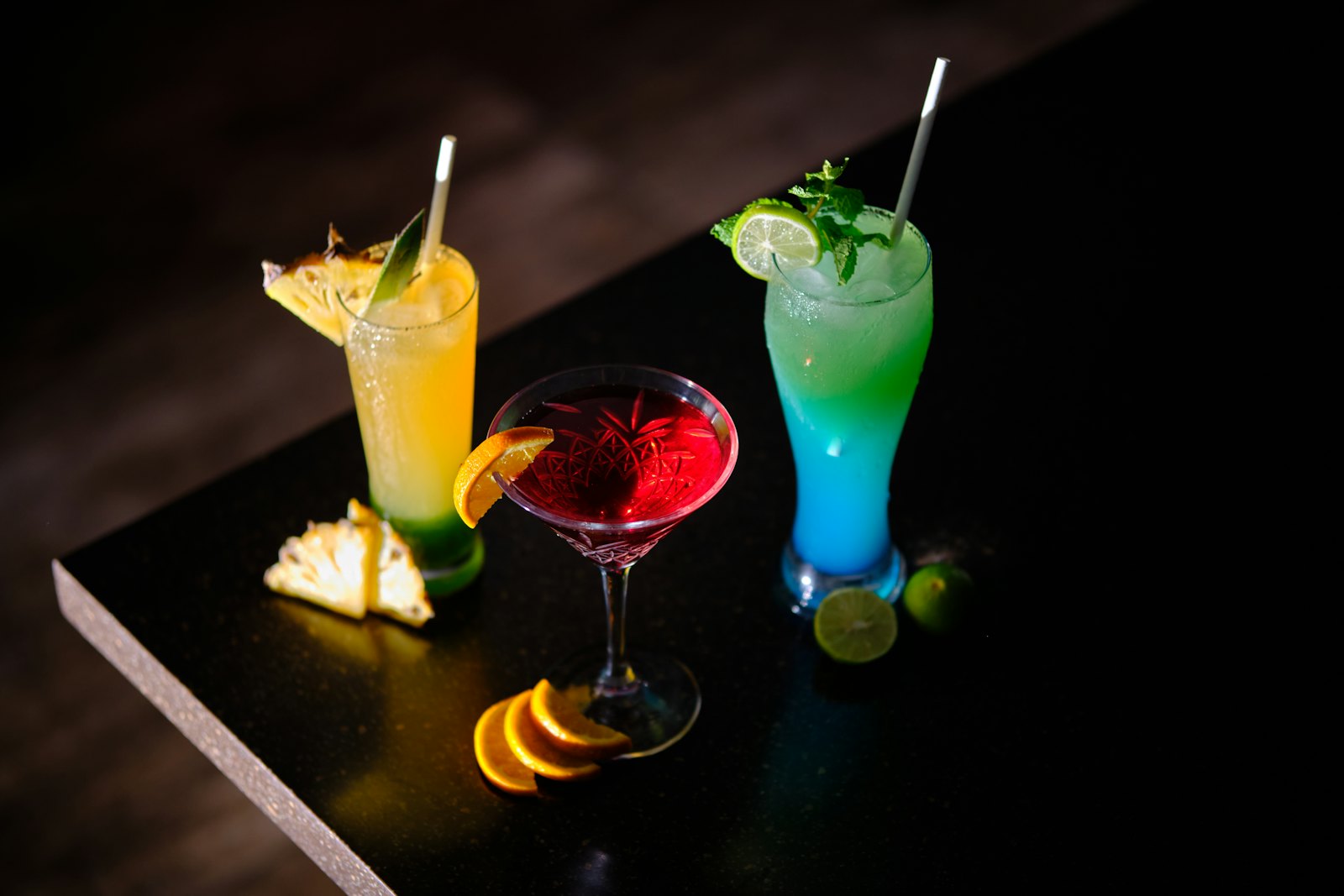 Three garnished cocktails lined up on a dark bar top